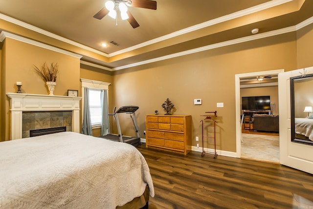 bedroom with a tray ceiling, a tiled fireplace, crown molding, and dark hardwood / wood-style flooring