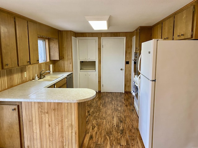 kitchen featuring kitchen peninsula, sink, white appliances, dark wood-type flooring, and wooden walls