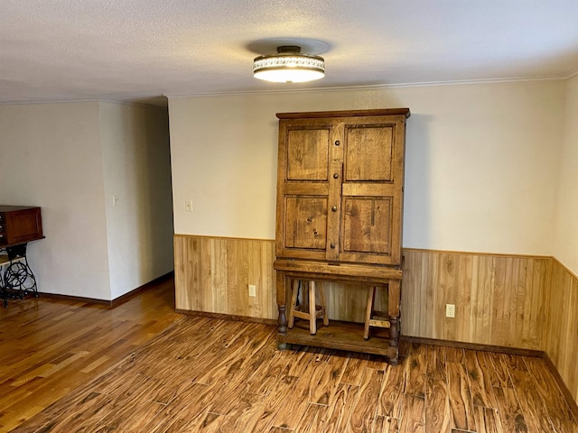 empty room featuring crown molding, dark hardwood / wood-style floors, a textured ceiling, and wooden walls