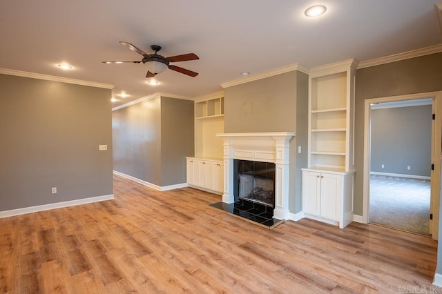 unfurnished living room featuring built in shelves, light hardwood / wood-style floors, a tiled fireplace, crown molding, and ceiling fan