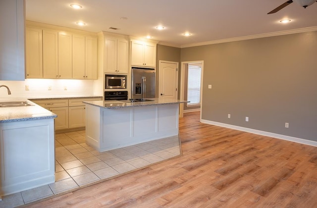 kitchen with appliances with stainless steel finishes, a kitchen island, sink, and white cabinetry