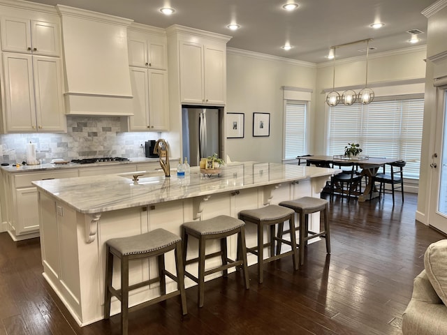 kitchen featuring a center island with sink, stainless steel appliances, white cabinets, a sink, and premium range hood