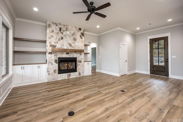 unfurnished living room featuring light wood-type flooring, ceiling fan, crown molding, and a stone fireplace