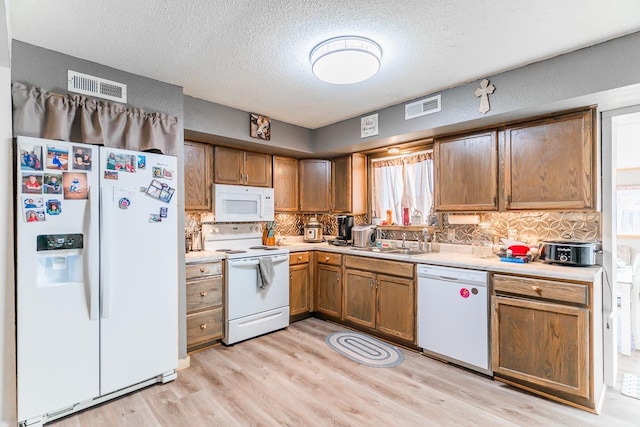 kitchen featuring tasteful backsplash, white appliances, a textured ceiling, light hardwood / wood-style floors, and sink