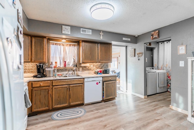 kitchen with washing machine and dryer, light hardwood / wood-style flooring, sink, backsplash, and white appliances