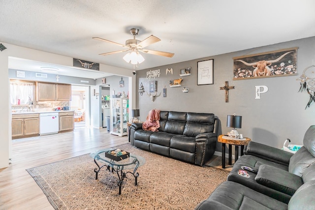 living room with light wood-type flooring, ceiling fan, and a textured ceiling