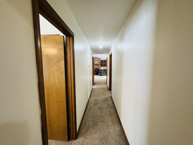 hallway with a textured ceiling and light colored carpet