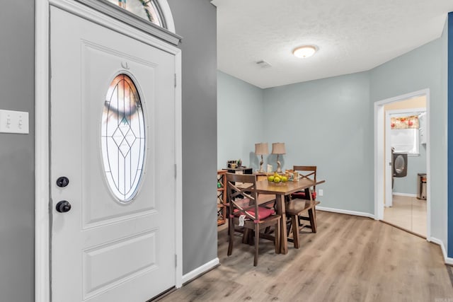 foyer with light wood-style floors, baseboards, and a textured ceiling