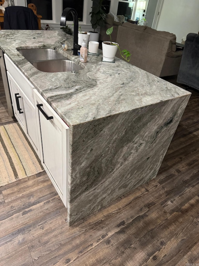 kitchen with dark wood finished floors, open floor plan, white cabinets, a sink, and light stone countertops