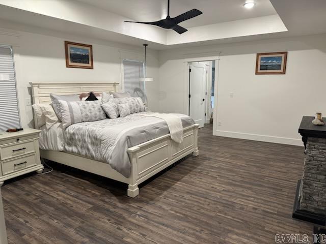 bedroom with a raised ceiling, dark wood finished floors, baseboards, and ceiling fan