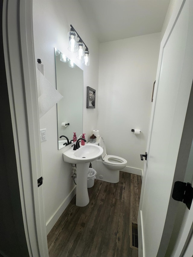 half bath featuring toilet, wood finished floors, visible vents, and baseboards