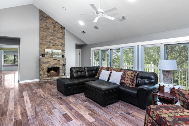 living room featuring high vaulted ceiling, a wealth of natural light, wood-type flooring, and a stone fireplace