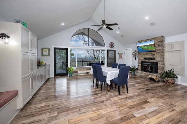 dining space featuring ceiling fan, light hardwood / wood-style flooring, a stone fireplace, and high vaulted ceiling