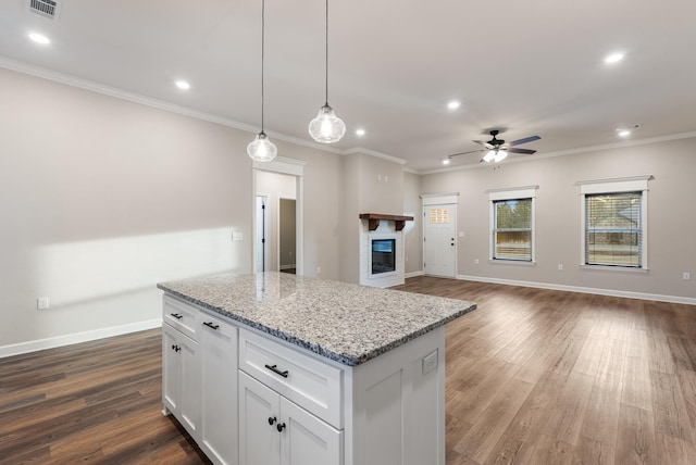 kitchen with pendant lighting, dark wood-type flooring, white cabinets, light stone countertops, and ornamental molding