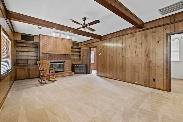 unfurnished living room featuring a brick fireplace, beamed ceiling, wood walls, and light colored carpet