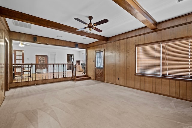 carpeted spare room featuring wooden walls, ceiling fan, and beam ceiling