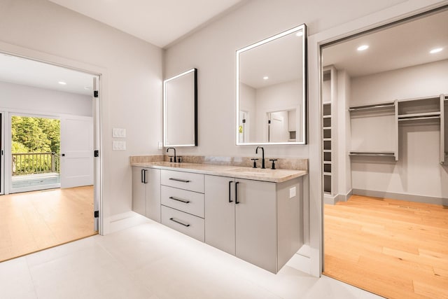 full bath featuring double vanity, wood finished floors, a walk in closet, and a sink