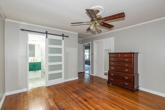 unfurnished room featuring ceiling fan, a barn door, dark wood-style flooring, baseboards, and crown molding