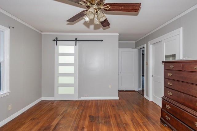 unfurnished bedroom with crown molding, dark wood finished floors, a barn door, a ceiling fan, and baseboards