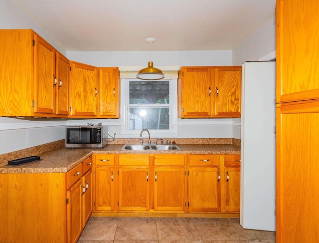 kitchen featuring stainless steel microwave, a sink, freestanding refrigerator, brown cabinetry, and pendant lighting