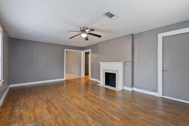 unfurnished living room featuring dark wood-type flooring, a tiled fireplace, visible vents, and baseboards