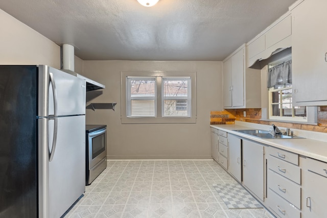 kitchen featuring stainless steel appliances, light countertops, white cabinets, a sink, and plenty of natural light