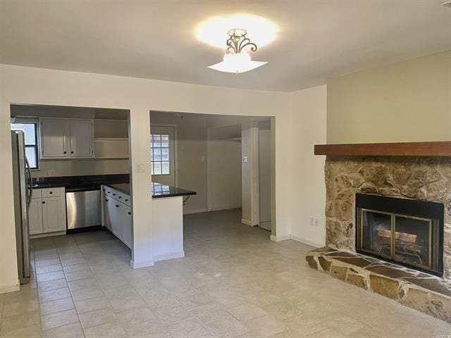 kitchen featuring a fireplace, stainless steel appliances, dark countertops, white cabinetry, and baseboards