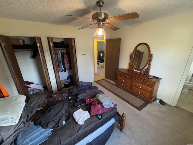 bedroom featuring a ceiling fan, light carpet, a textured ceiling, and two closets