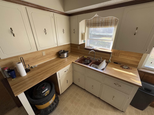 kitchen featuring light floors, light countertops, decorative backsplash, white cabinets, and a sink