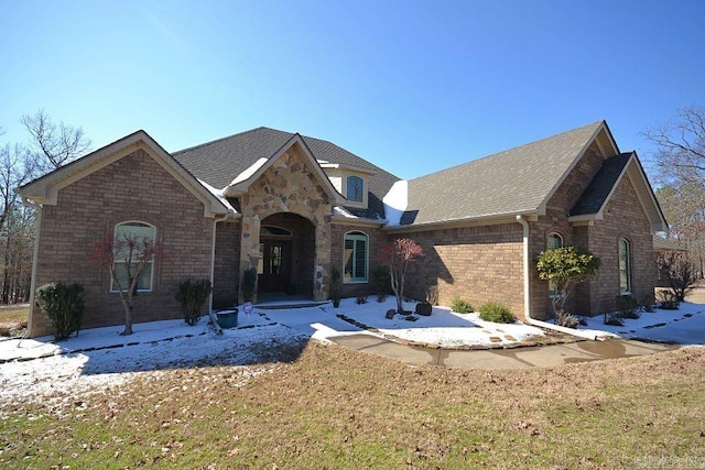 view of front of home featuring roof with shingles, a front lawn, and brick siding