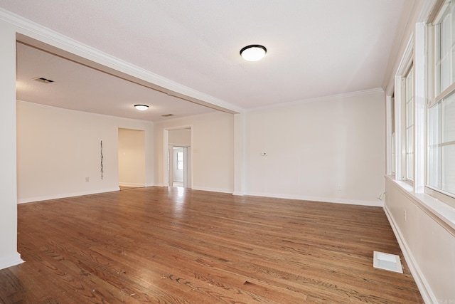 empty room with baseboards, visible vents, crown molding, and wood finished floors