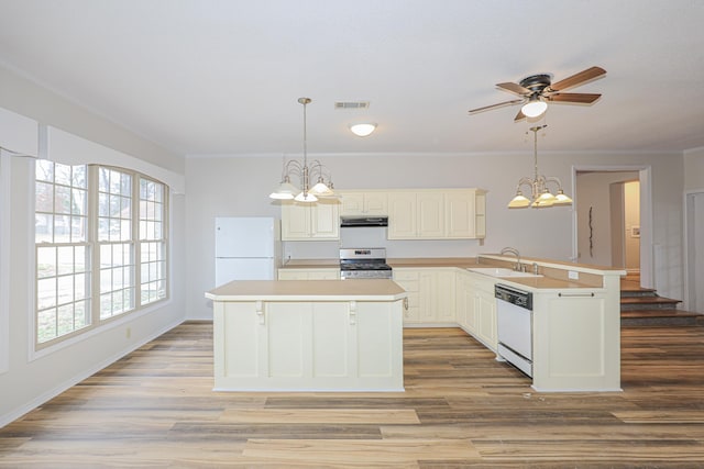 kitchen featuring a peninsula, white appliances, a sink, light countertops, and decorative light fixtures