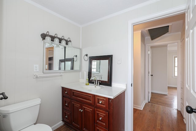 half bathroom featuring toilet, crown molding, wood finished floors, and vanity