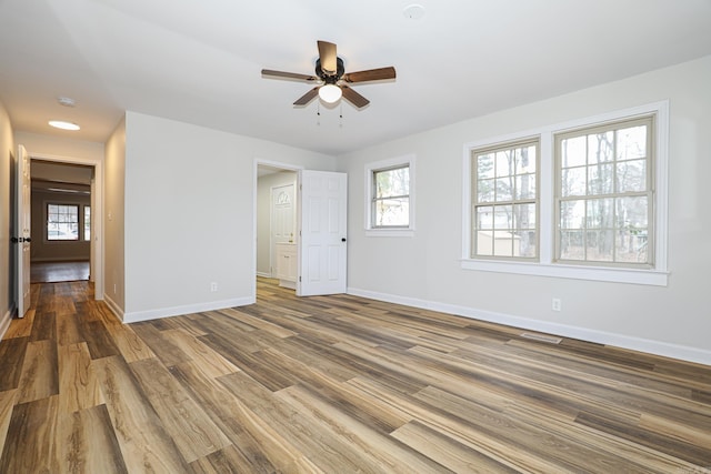 spare room with a ceiling fan, wood finished floors, a wealth of natural light, and baseboards