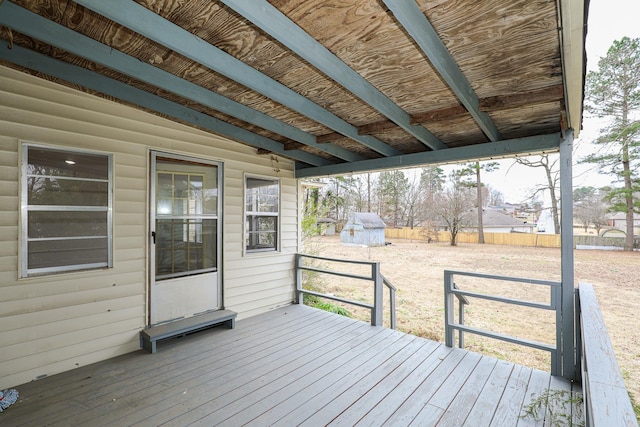 wooden deck featuring a shed, fence, and an outbuilding