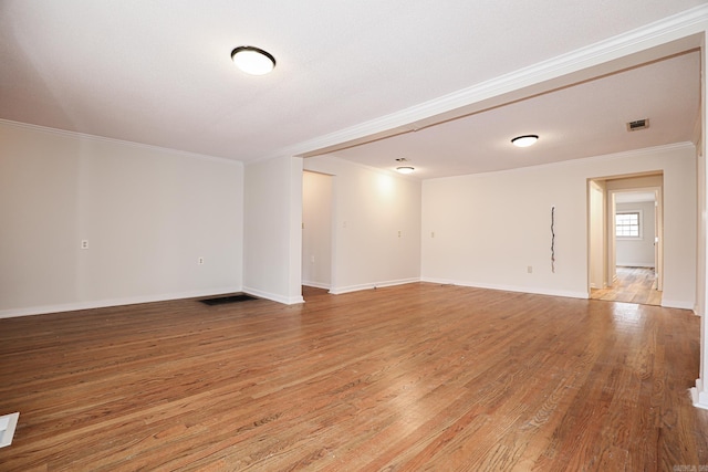 spare room with baseboards, wood finished floors, visible vents, and crown molding