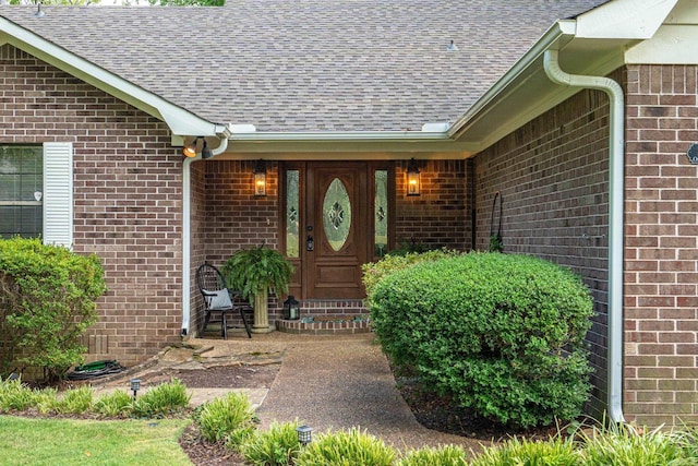 entrance to property featuring a shingled roof and brick siding