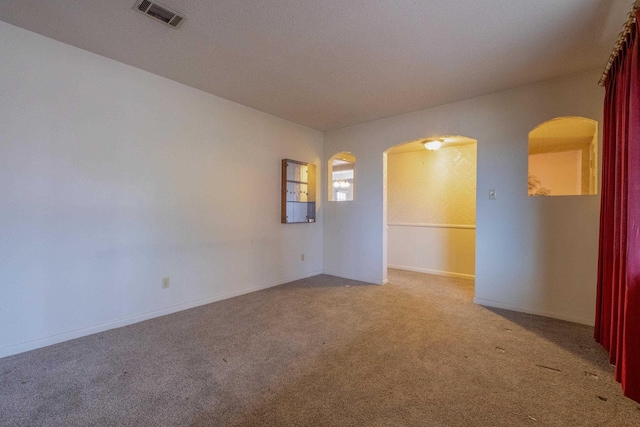 empty room featuring light carpet, baseboards, visible vents, and arched walkways