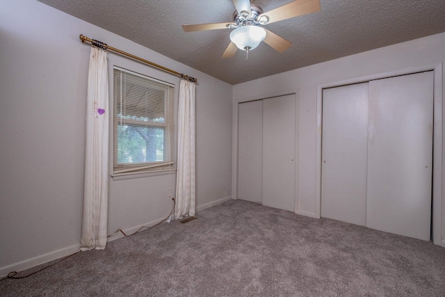 unfurnished bedroom with light carpet, ceiling fan, a textured ceiling, and two closets