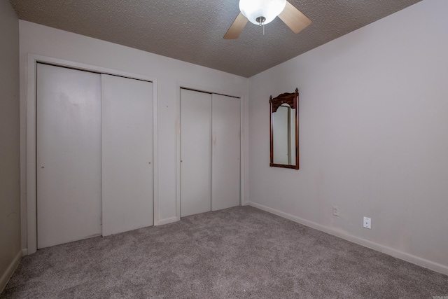 unfurnished bedroom with a textured ceiling, a ceiling fan, multiple closets, and light colored carpet