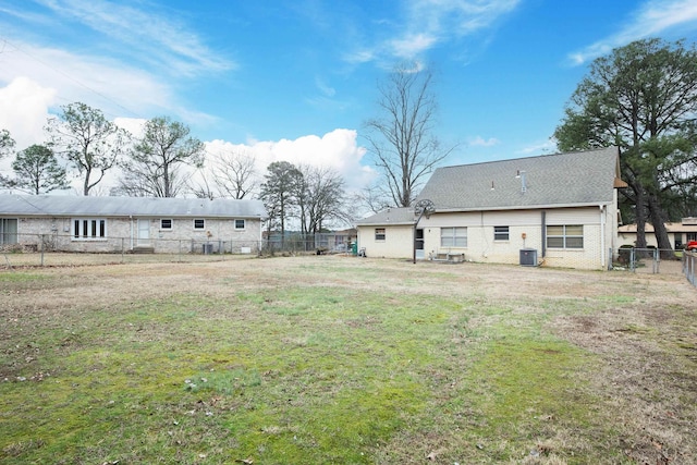 back of property featuring central AC unit, brick siding, fence, and a yard