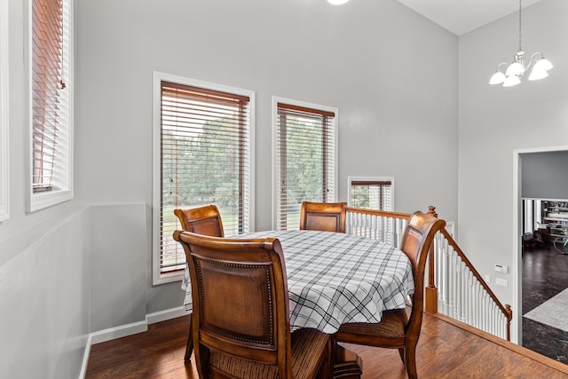 dining space featuring a notable chandelier, dark wood finished floors, a towering ceiling, and baseboards