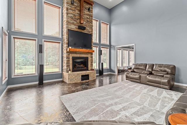 living area featuring finished concrete flooring, a high ceiling, baseboards, and a stone fireplace