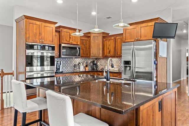 kitchen featuring stainless steel appliances, a sink, a center island with sink, and pendant lighting