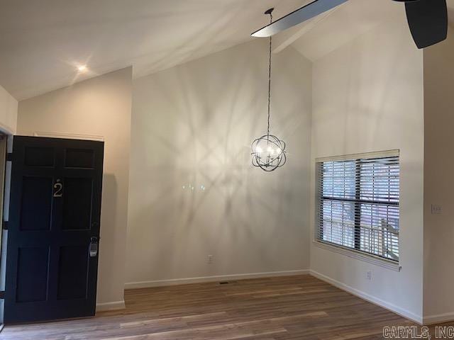 spare room with high vaulted ceiling, an inviting chandelier, baseboards, and wood finished floors