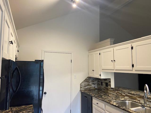 kitchen featuring a sink, white cabinetry, freestanding refrigerator, dark stone counters, and tasteful backsplash