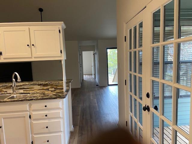 kitchen with dark wood-style floors, french doors, white cabinetry, a sink, and dark stone counters