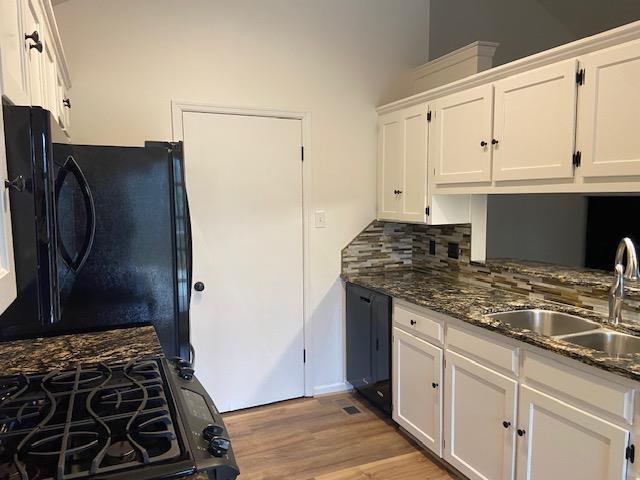 kitchen with light wood finished floors, tasteful backsplash, white cabinets, dark stone countertops, and a sink