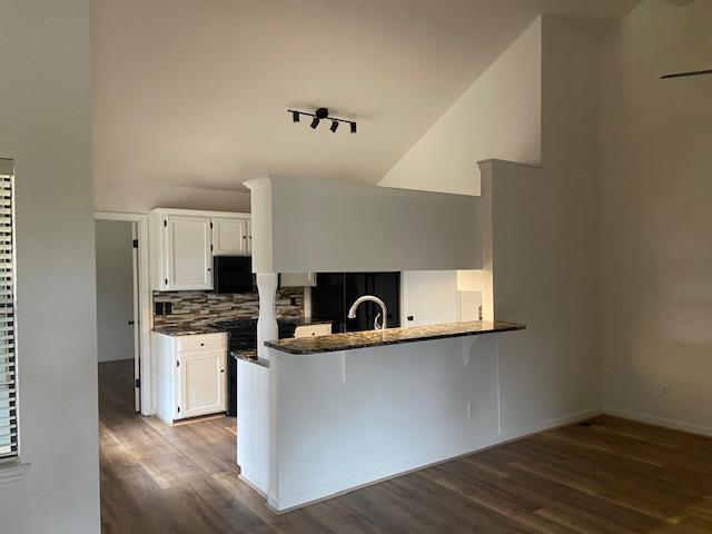 kitchen with a peninsula, dark wood-type flooring, backsplash, and white cabinetry