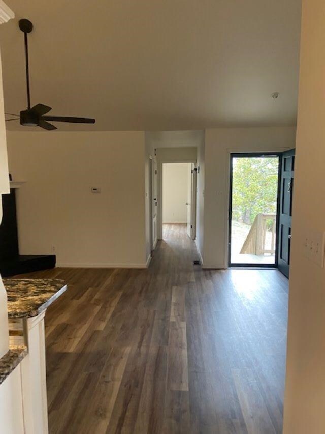 unfurnished living room with dark wood-type flooring, baseboards, and a ceiling fan